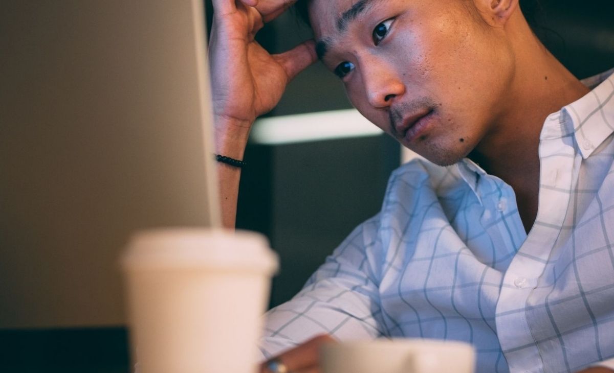An Asian man looks pensively at a laptop
