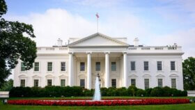 Picture of the United States White House, green lawn in the front and a water fountain erupting in the center.