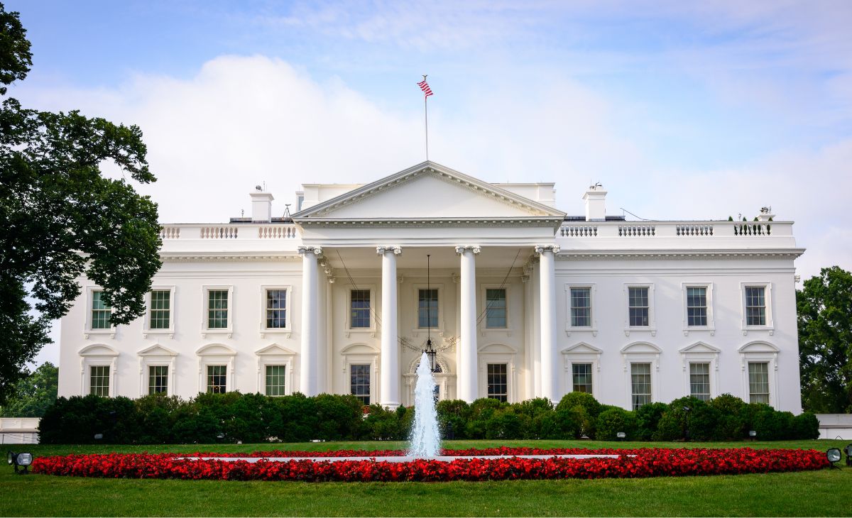 Picture of the United States White House, green lawn in the front and a water fountain erupting in the center.